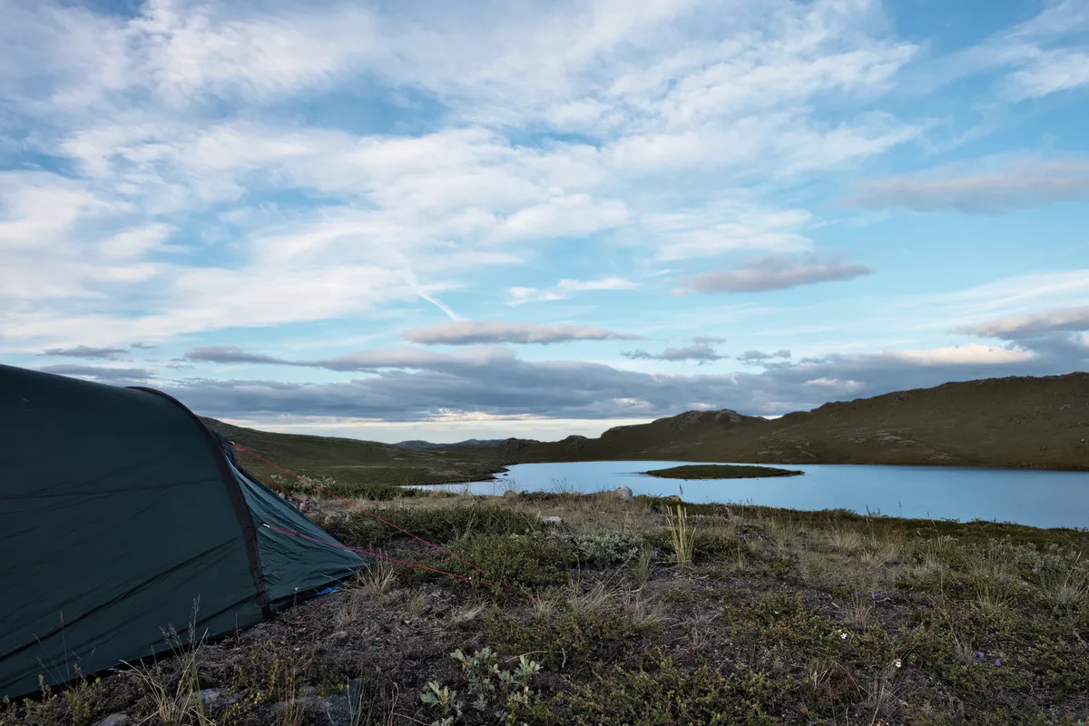 zelt in grönländischer tundra unter leicht bewölktem himmel an einem see